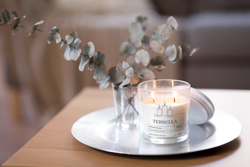 Image of a white candle in a glass jar. the jar shows a clear label detailing the fragrance and brand of candle. 