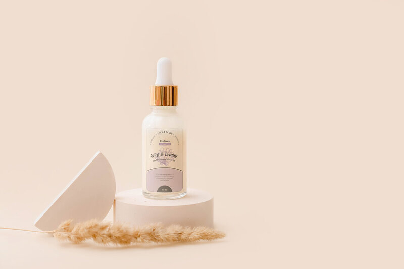 A bottle of beauty serum is artfully displayed on a pedestal. The bottle displays a clear label.