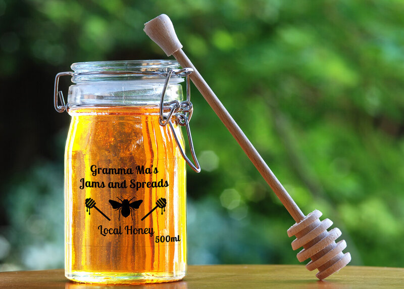 a large jar of honey sits on a table with trees in the background. The honey jar shows a clear label branded for a local canadian honey business.